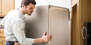 Electrician moving a fridge in a kitchen