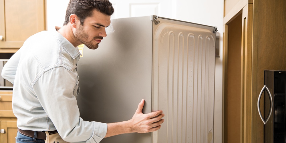 Electrician moving a fridge in a kitchen